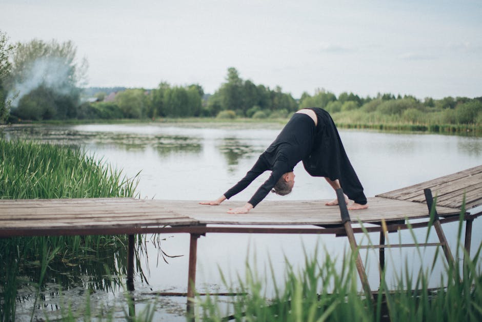 A woman in a calm yoga pose on a wooden deck surrounded by tranquil water and greenery.